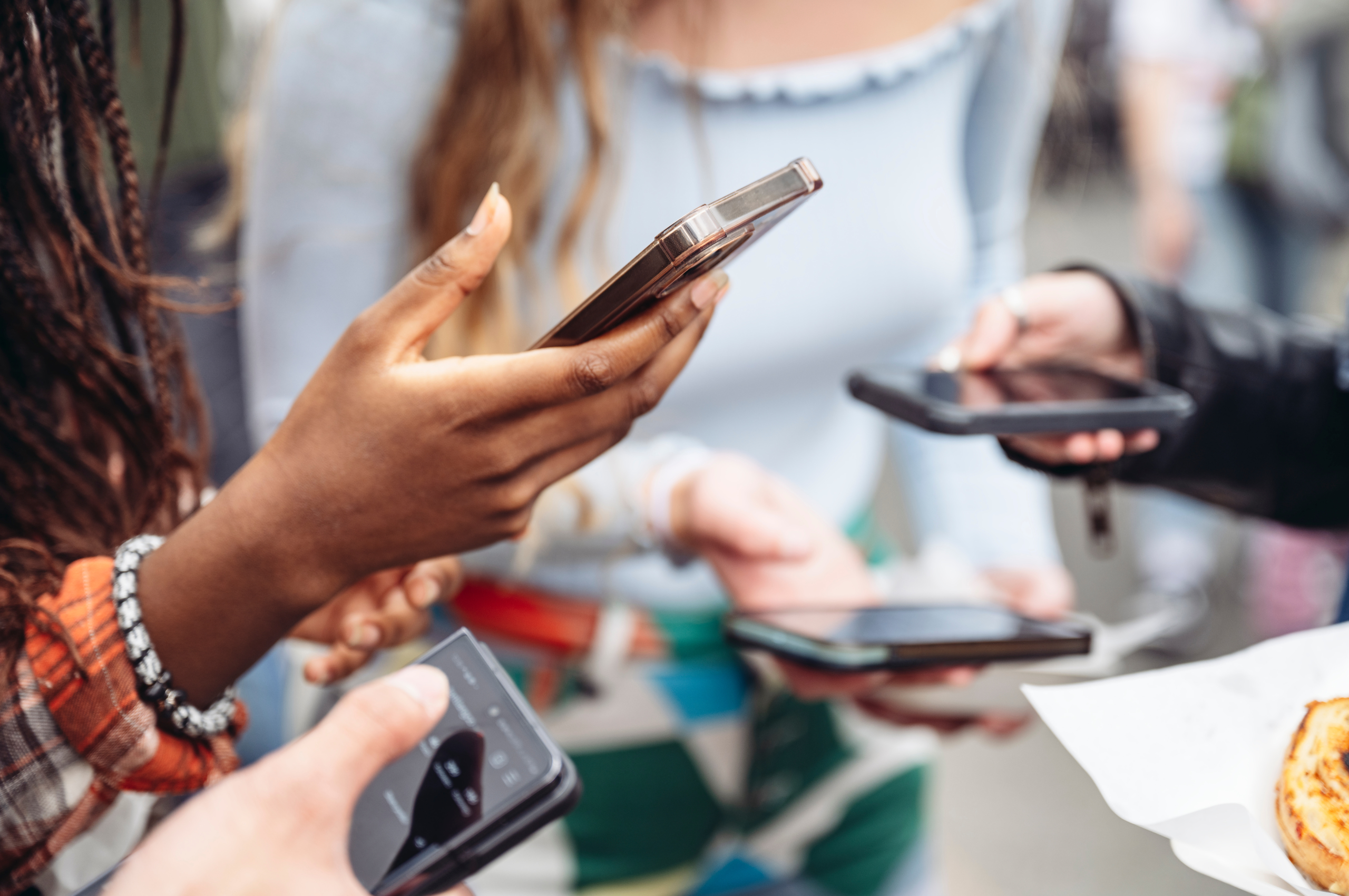 A imagem mostra diversas mãos segurando celulares. As pessoas na foto parecem ser jovens adultos - público frequentemente impactado pela falta de equilíbrio na relação entre redes sociais e saúde mental.